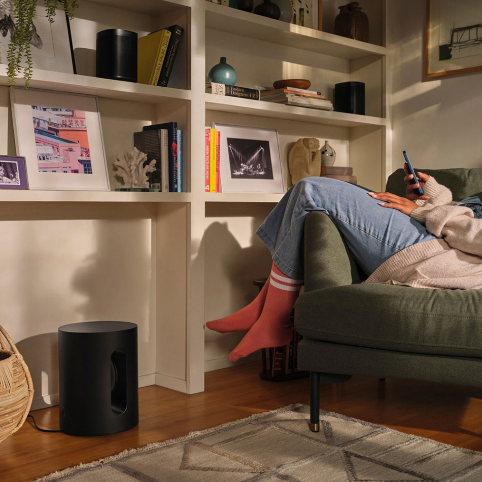 En person sitter i soffa med Sonos-högtalare och omgivande inredning i ett rum.