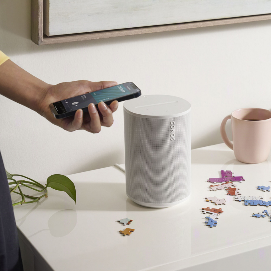 En person spelar musik med telefonen vid en vit Sonos-högtalare.