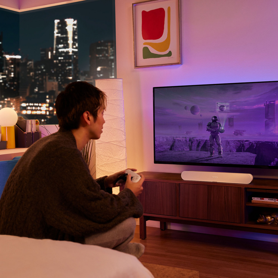 En person spelar videospel framför en TV med en Sonos Ray soundbar.