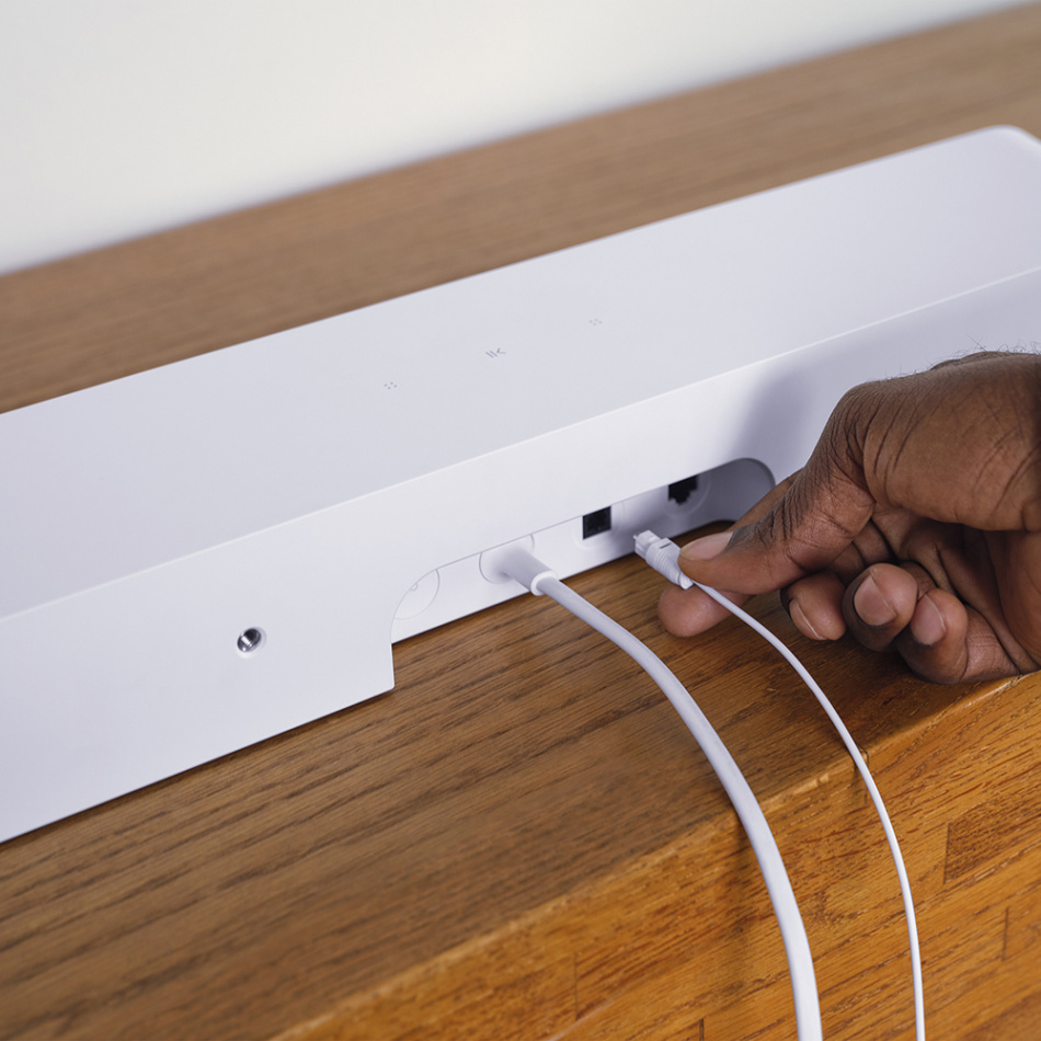En person kopplar in kablar på baksidan av en vit soundbar.