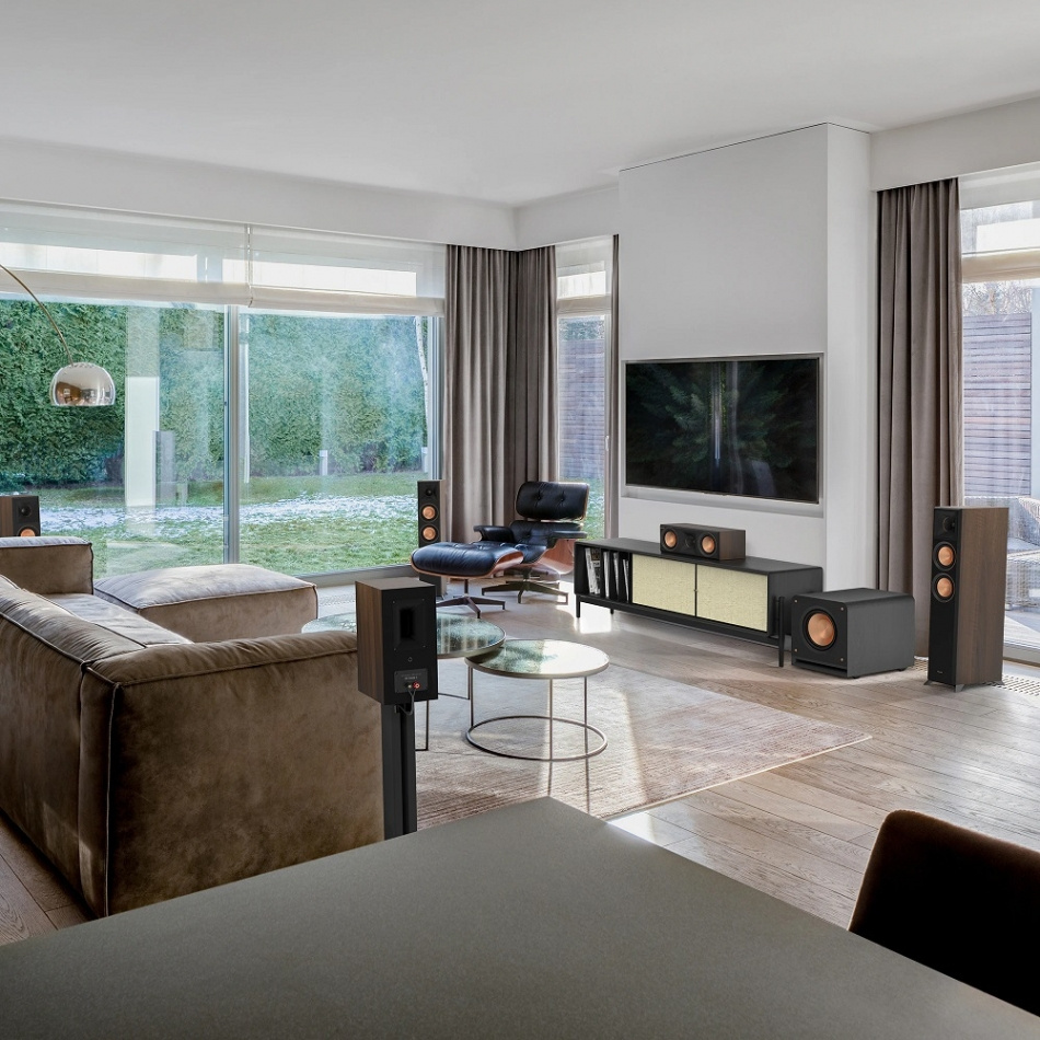 Modern vardagsrum med stora fönster, soffa och ljudsystem.