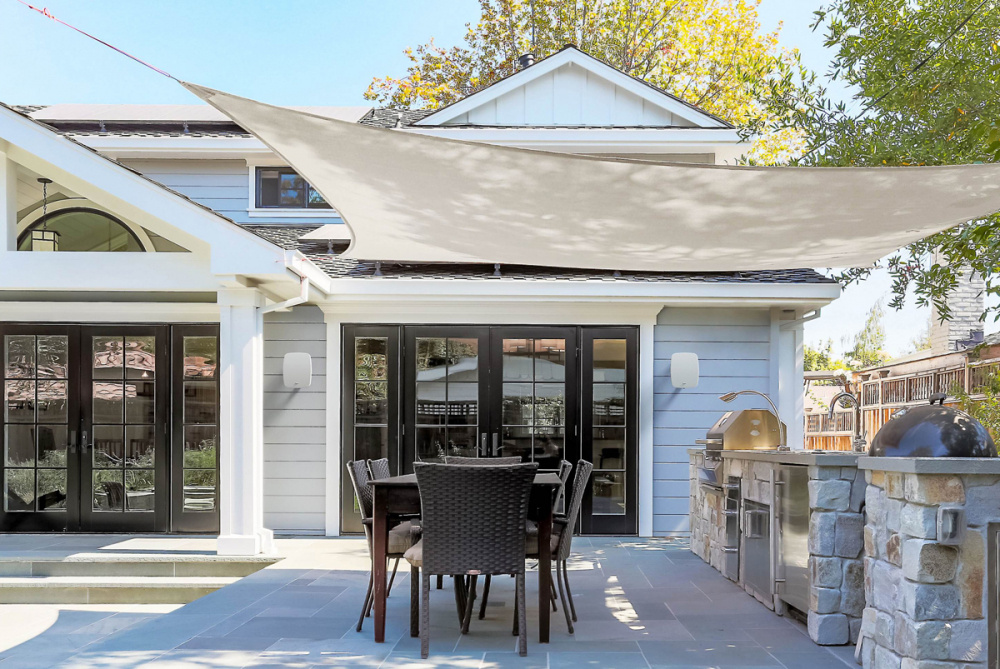 En modern uteplats med matgrupp och grill under ett solskydd.