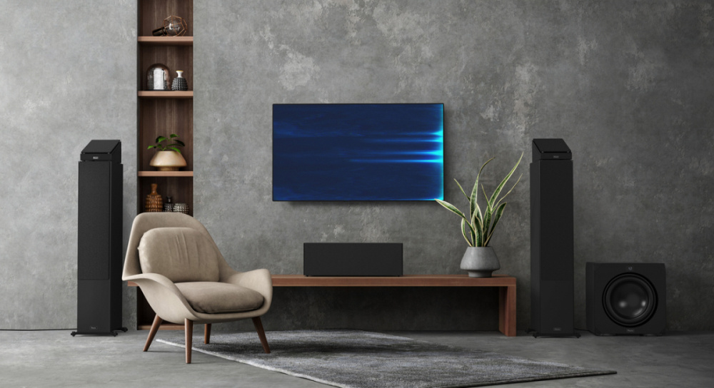 Svart högtalarpaket och TV i modern inredning med fåtölj och växt.