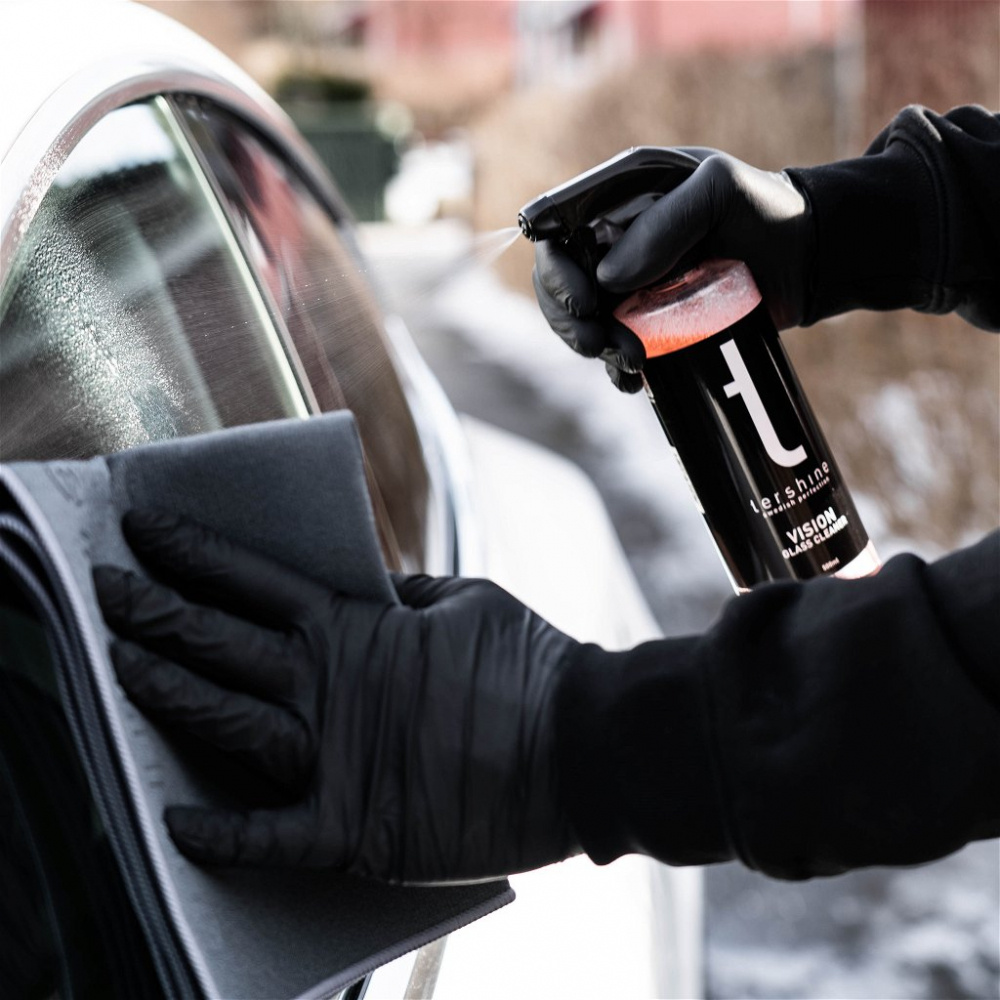 En person rengör en bilruta med glasrengöringsmedel och en mikrofiberduk.