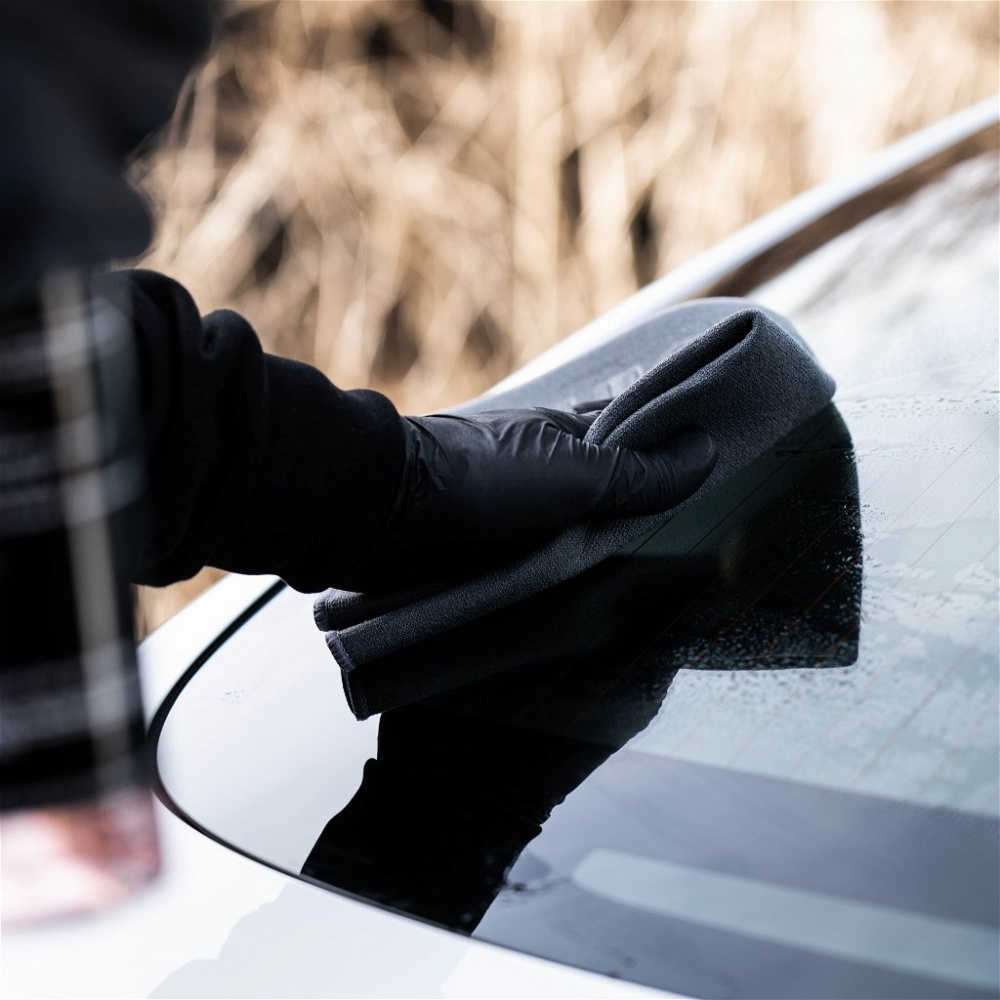 En person rengör en bilruta med en microfiberduk.