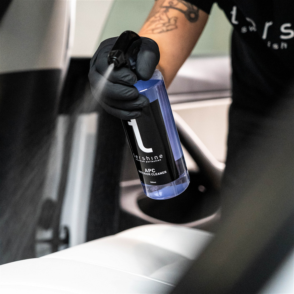 En person sprayar en rengöringsprodukt på en vit yta i bilinteriören.