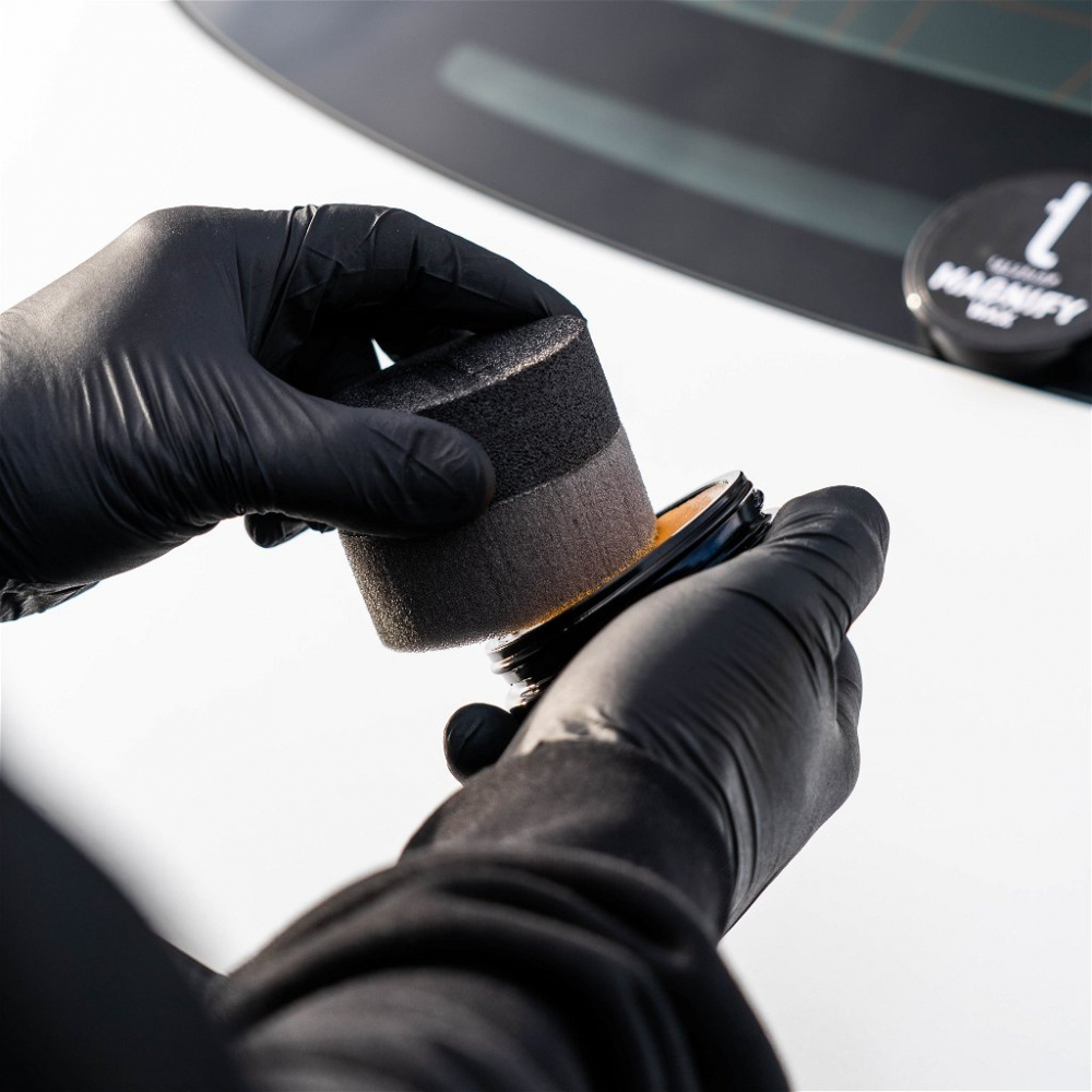 En hand som håller en poleringskudde och burk med vax.