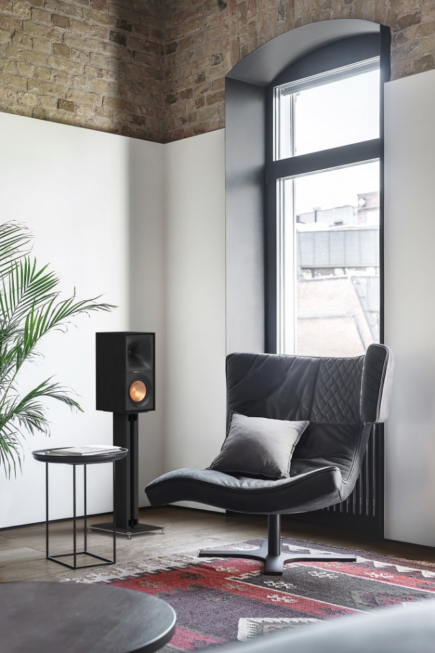 Snygg inredning med en stol, högtalare och en växt vid ett fönster.